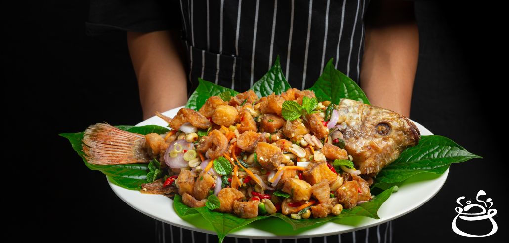 Chef holding a plate of garnished fried fish with vegetables and herbs